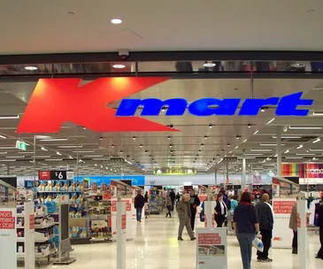 Kmart store entrance with shoppers inside, bright signage and retail items displayed.