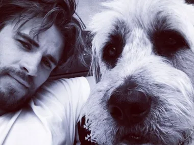A man takes a close-up selfie with a large fluffy dog, both looking into the camera.
