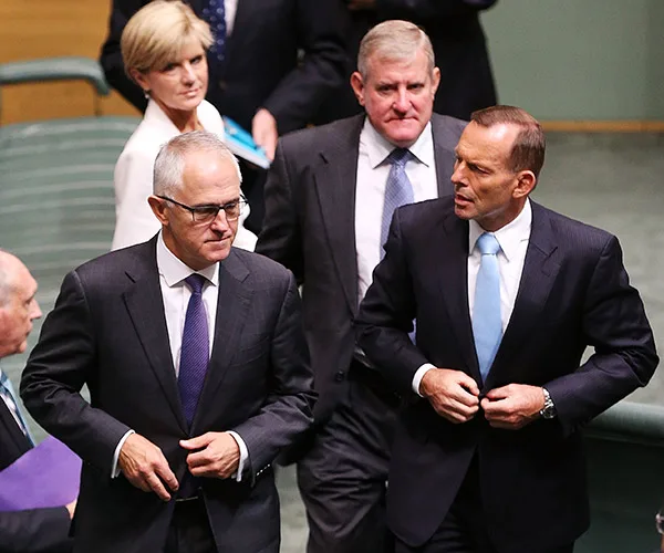 Political figures in suits walking and conversing in a formal setting.