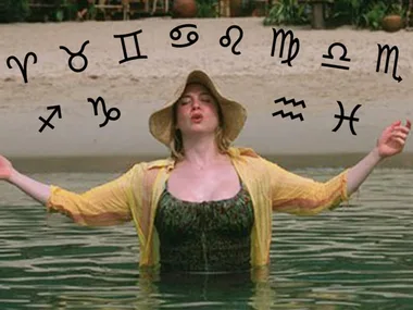 Person in water with a hat and open arms under zodiac symbols on a beach.