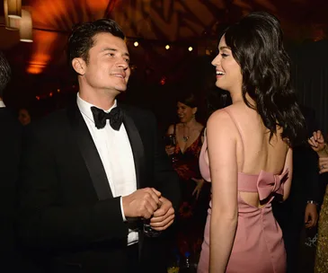 Two people smiling and chatting at an event, wearing formal attire, with a lively crowd in the background.