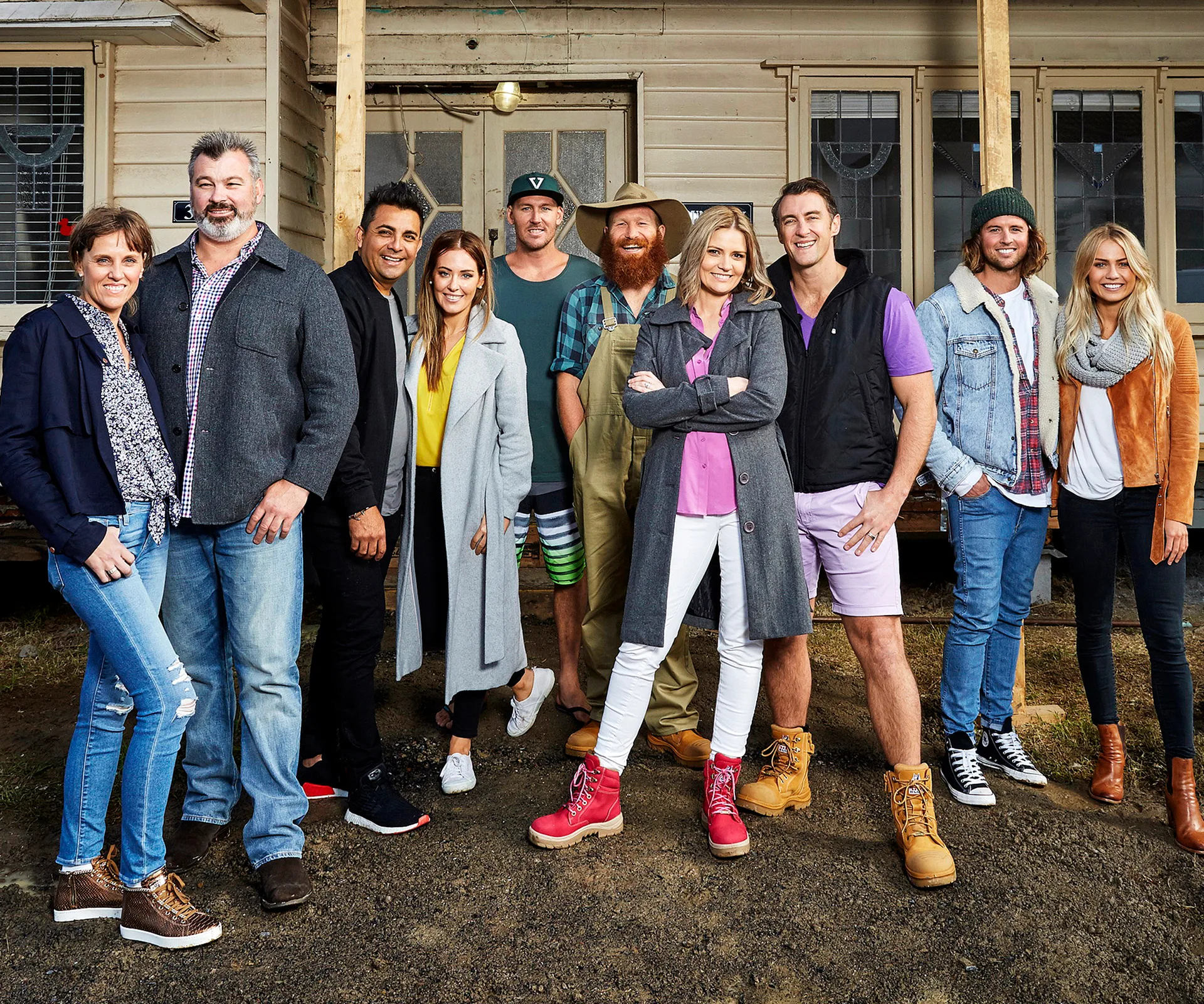 Group of ten people posing outside a rustic house, dressed in casual and winter clothing.