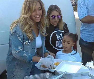 Beyoncé and a child help distribute food to Hurricane Harvey victims.