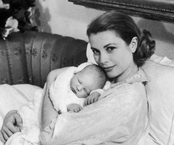 A mother sweetly holding a sleeping newborn in her arms, lying on a couch with flowers in the background.
