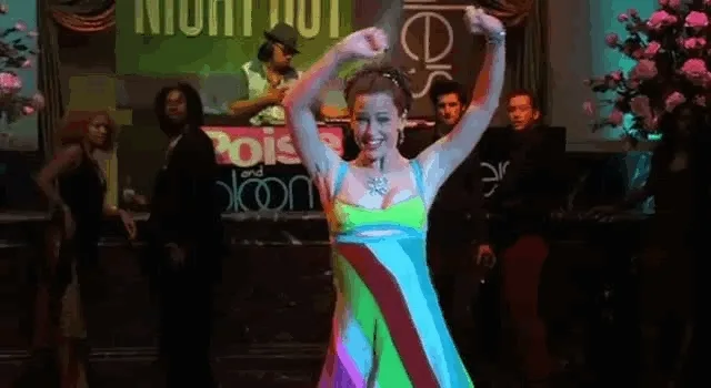 Colorful-dressed woman dancing at a lively party with a DJ in the background.
