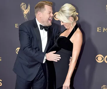 Man in tuxedo and woman in black dress smiling, standing close on the red carpet at the Emmys 2017.