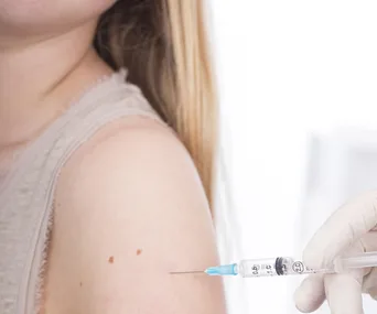 A child receiving a vaccination shot in the upper arm; medical syringe with gloved hand.