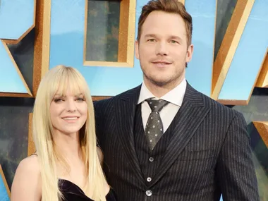 A woman in a black dress with long blonde hair stands beside a man in a pinstripe suit and tie at an event.