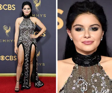 "Person in a glittering dress with high slits, standing on a red carpet at an award event."
