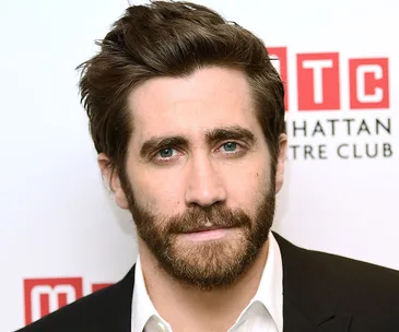 A man with a beard and styled hair in a suit at a Manhattan Theatre Club event backdrop.