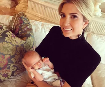 A woman smiling while holding a newborn baby on a patterned couch.