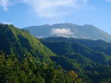 Lush green hills with a clear view of a volcano in the background under a blue sky.
