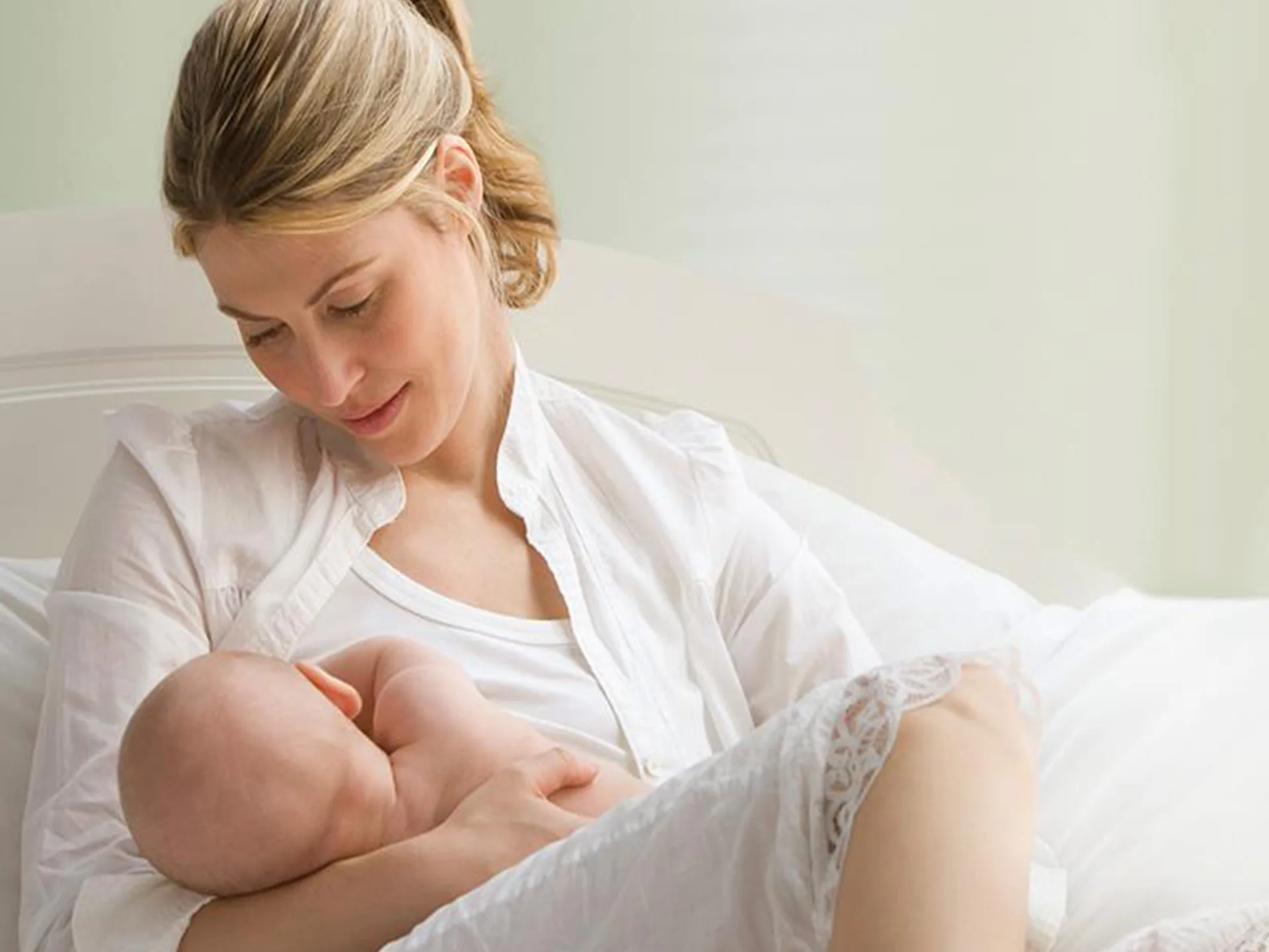 A mother tenderly breastfeeding her baby while sitting on a bed, exuding warmth and care.