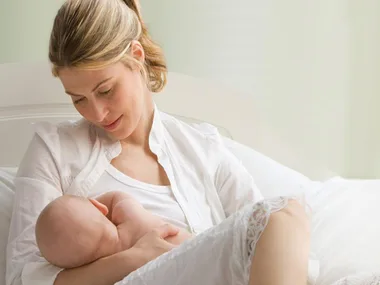 A mother tenderly breastfeeding her baby while sitting on a bed, exuding warmth and care.