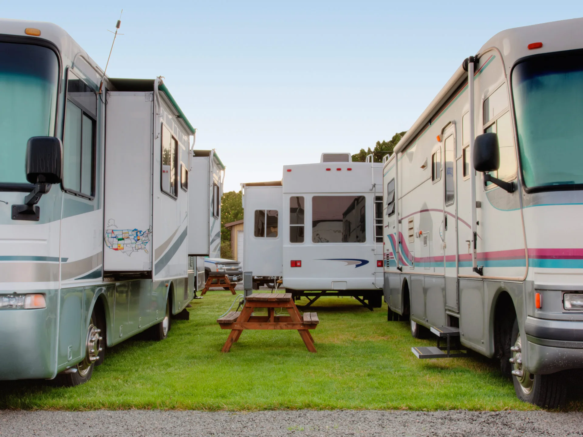 RVs parked closely in a grassy caravan park, with picnic tables positioned between them.