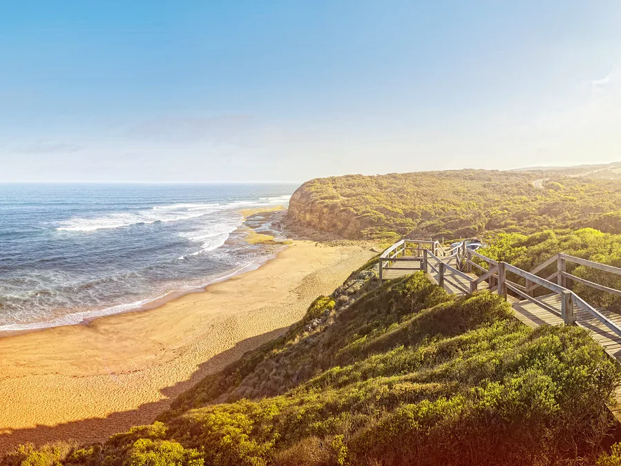 Rugged coastline view of Bells Beach, Australia with sandy shores, ocean waves, and a wooden boardwalk.