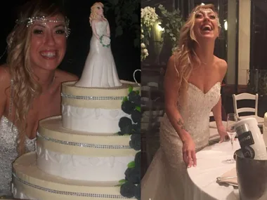 Smiling woman in wedding dress next to cake with bride topper, celebrating her unique ceremony.