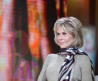A person with short hair and a striped scarf, standing in front of a colorful, blurred background.