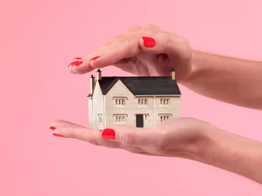 Hands with red nails holding a model house, symbolizing home protection.
