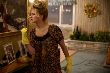 Woman in leopard print dress and yellow gloves cleaning a vintage-style living room.