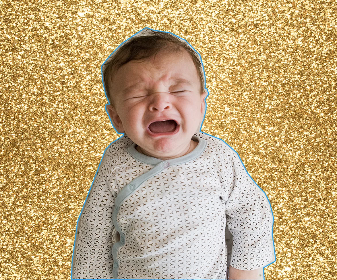 Crying baby in patterned outfit against a glittery gold background.