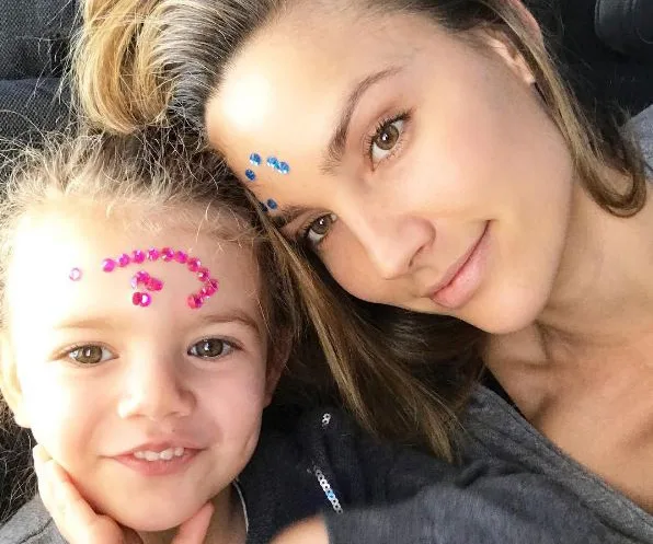 A woman and child with decorative gems on their foreheads, smiling closely together, in a relaxed setting.
