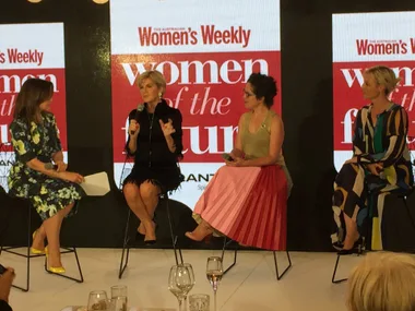 Panel discussion at Women's Weekly event, four women seated, one speaking, in front of "Women of the Future" backdrop.