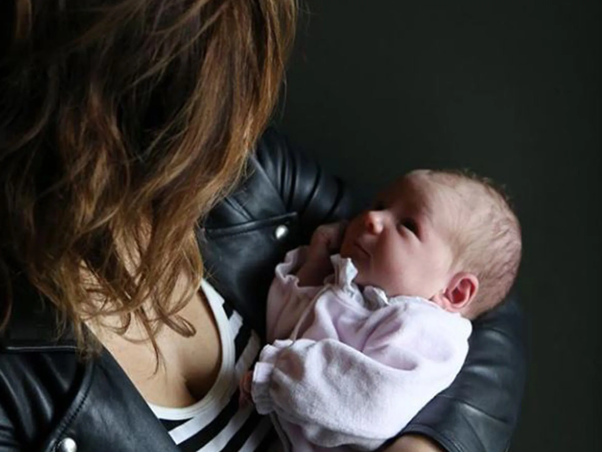 A woman in a striped shirt holds a newborn, both gazing at each other with affection.