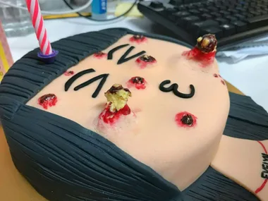 A cake of a face with realistic acne, black hair, and a red candle adhered.