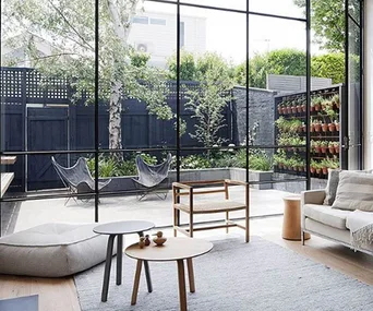 Open-plan living room with minimalist furniture, large windows, and garden view. Neutral tones with abundant natural light.