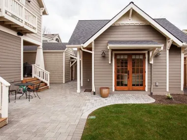 Granny pod with wooden doors, patio furniture, and brick walkway in backyard setting.