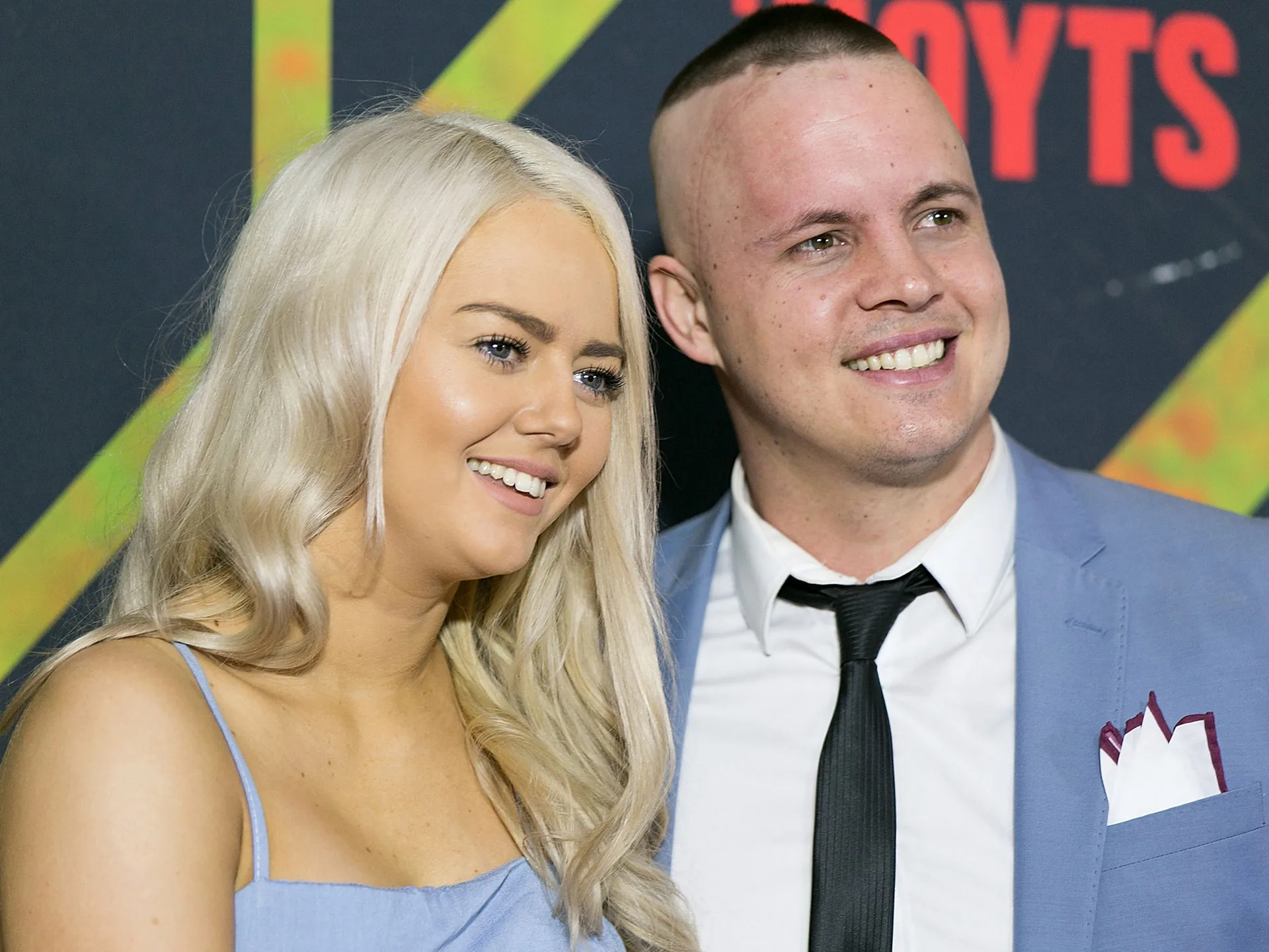 Two people smiling at a public event, man wearing a blue suit, woman in a blue dress.