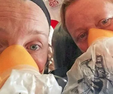 Two passengers wearing oxygen masks on an airplane.