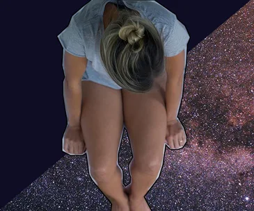 A woman in a gray shirt sits with head down on a starry background, representing a feeling of sadness or contemplation.