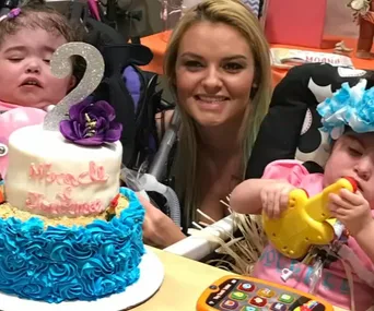 A birthday celebration featuring two children and an adult with a cake that reads "Miracle and Madness."