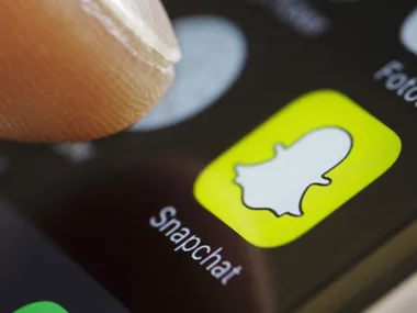 Close-up of a finger hovering over the Snapchat app icon on a smartphone screen.