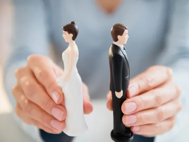 Hands holding wedding cake topper figurines of a bride and groom facing away from each other.