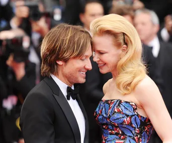 Celebrity couple smiling closely on a red carpet, wearing formal attire.