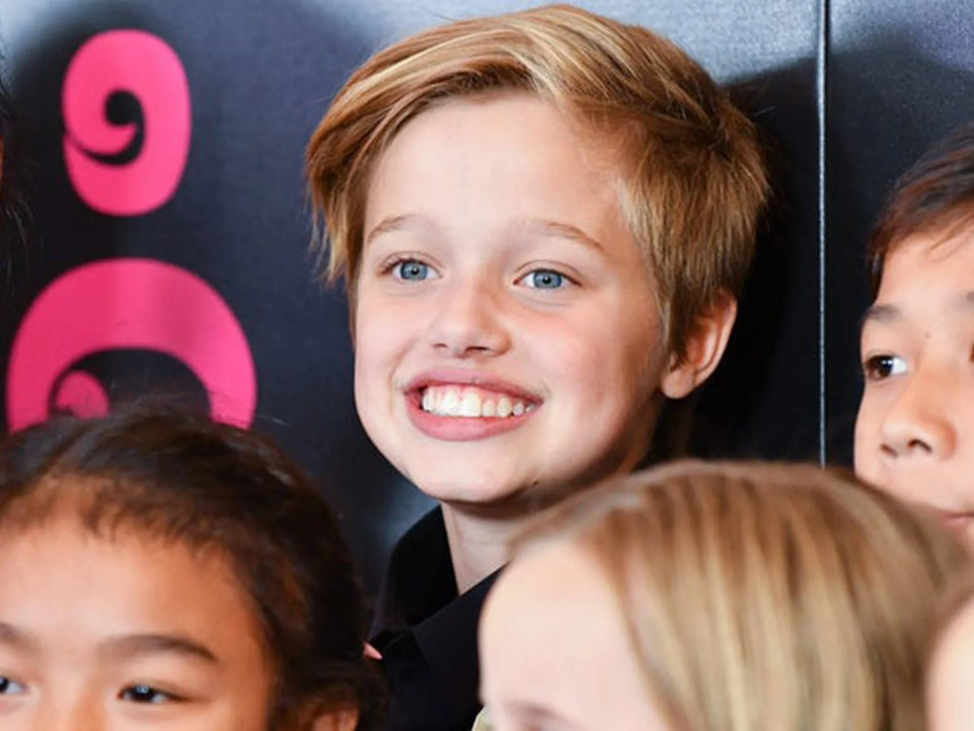 Group of children smiling at an event, with a colorful background featuring abstract circular designs.