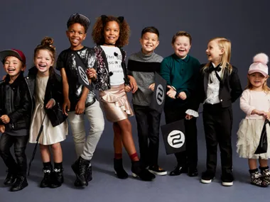 Children posing joyfully in diverse stylish outfits for River Island campaign against a dark backdrop.
