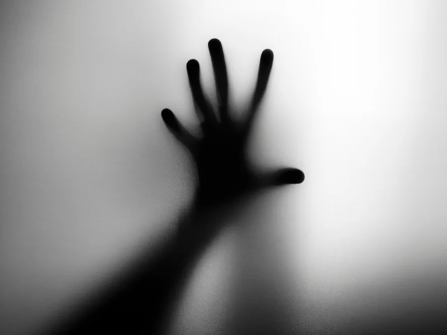 A silhouetted hand pressed against frosted glass, evoking a spooky, haunted ambiance.