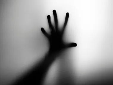 A silhouetted hand pressed against frosted glass, evoking a spooky, haunted ambiance.