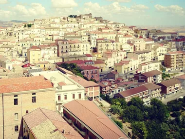 Aerial view of a picturesque Italian hill town with tightly packed buildings and red-tiled roofs under a blue sky.