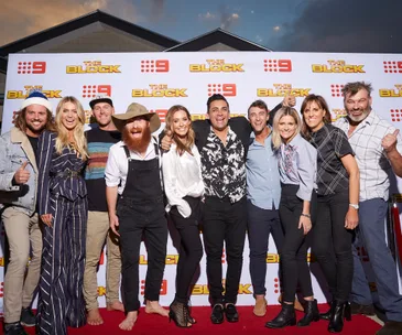 Group of people smiling on the red carpet at an event for "The Block," standing against a branded backdrop.