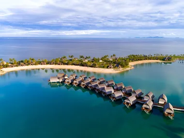 Aerial view of luxurious overwater bungalows and tropical palm-lined islands at a Fiji resort.