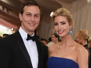 A couple dressed formally, smiling at an event, with the woman in a blue dress and statement earrings.