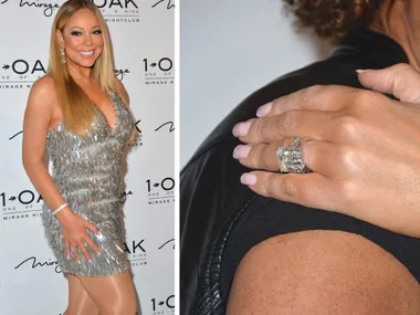Woman in a silver dress posing with a large engagement ring on her finger at an event backdrop.