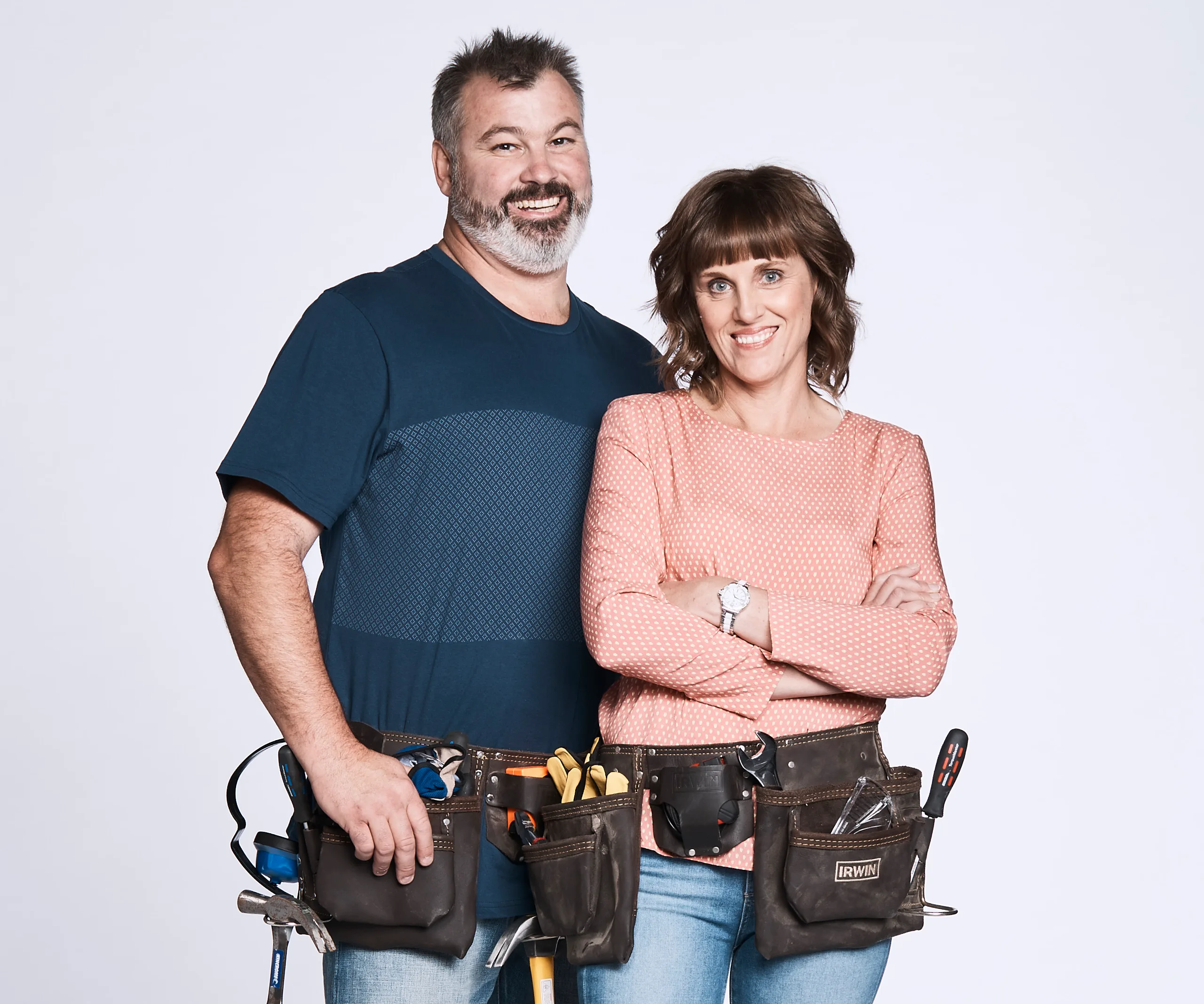 A couple from "The Block 2017," both wearing tool belts, smiling confidently at the camera.