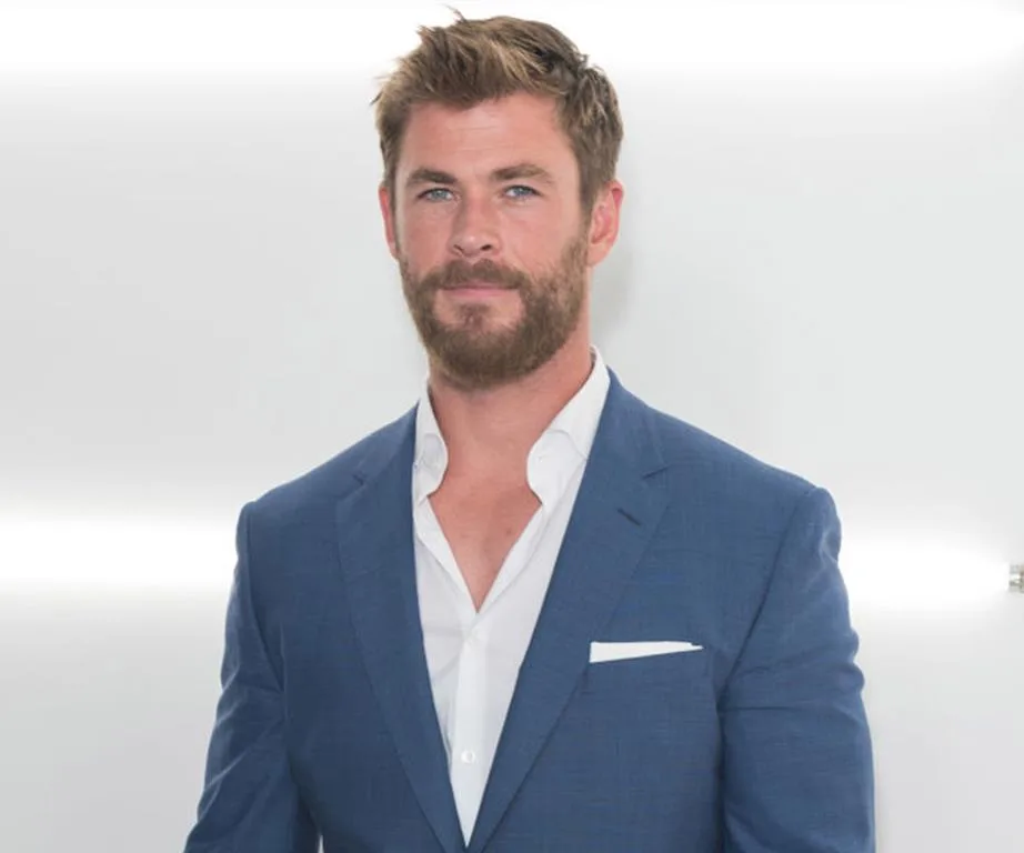 Man in a blue suit with a beard and light hair, standing, against a white background.