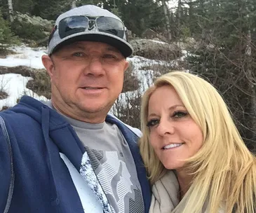 A smiling couple taking a selfie outdoors in a snowy forest setting.